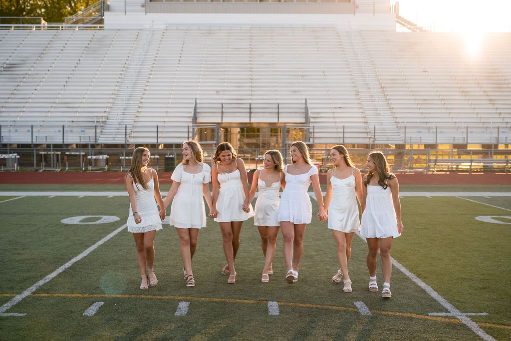 Group of cheerleaders in white uniforms practicing formations on a football field at sunset.