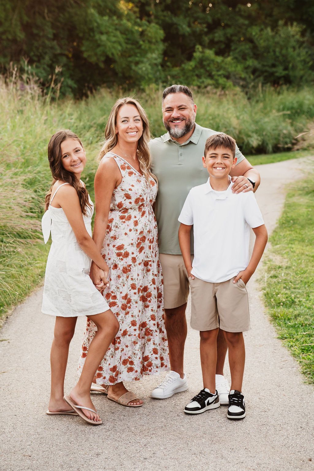 Happy family of four posing on a scenic path surrounded by lush greenery during an outdoor photo session.