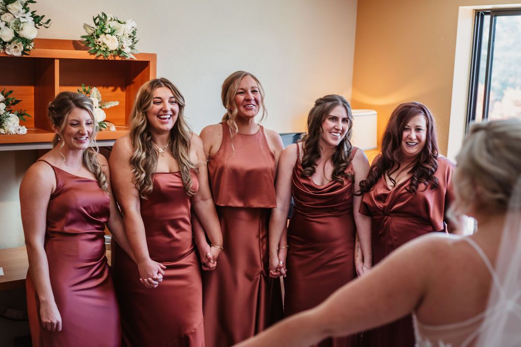 Bridesmaids in matching burgundy dresses share joyful moment during wedding preparations.
