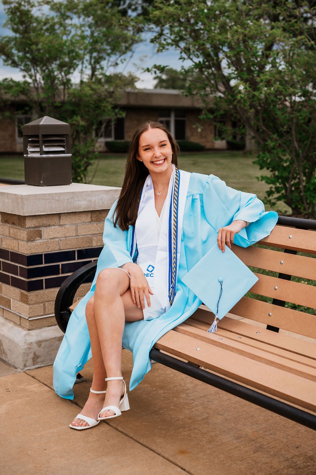 A series of outdoor photos showing someone in a light blue graduation gown sitting on a wooden bench.