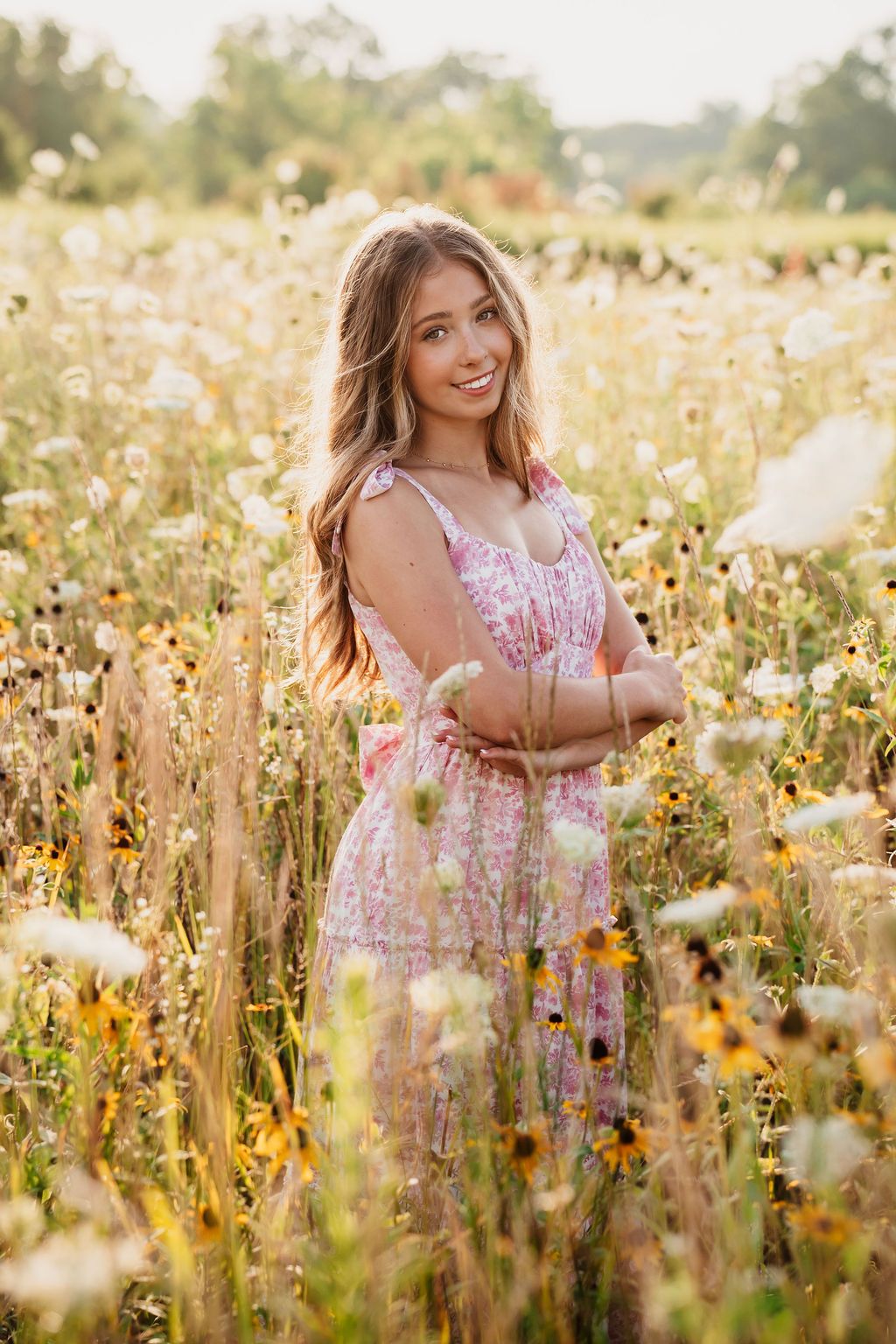 A golden wildflower field at sunset with a person in a pink floral dress enjoying the warm summer evening.