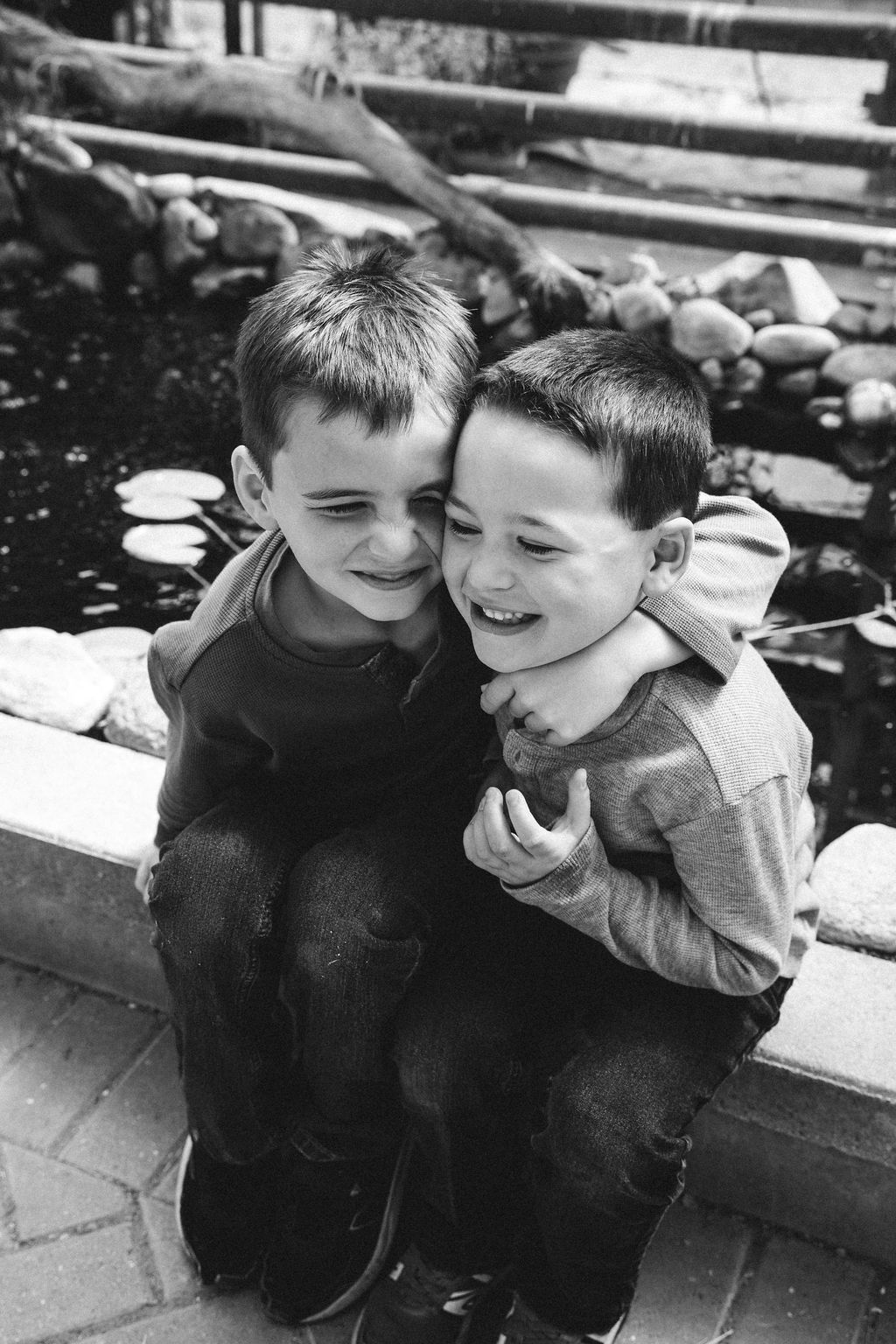 Two young boys laughing and hugging by a garden pond in black and white photo.