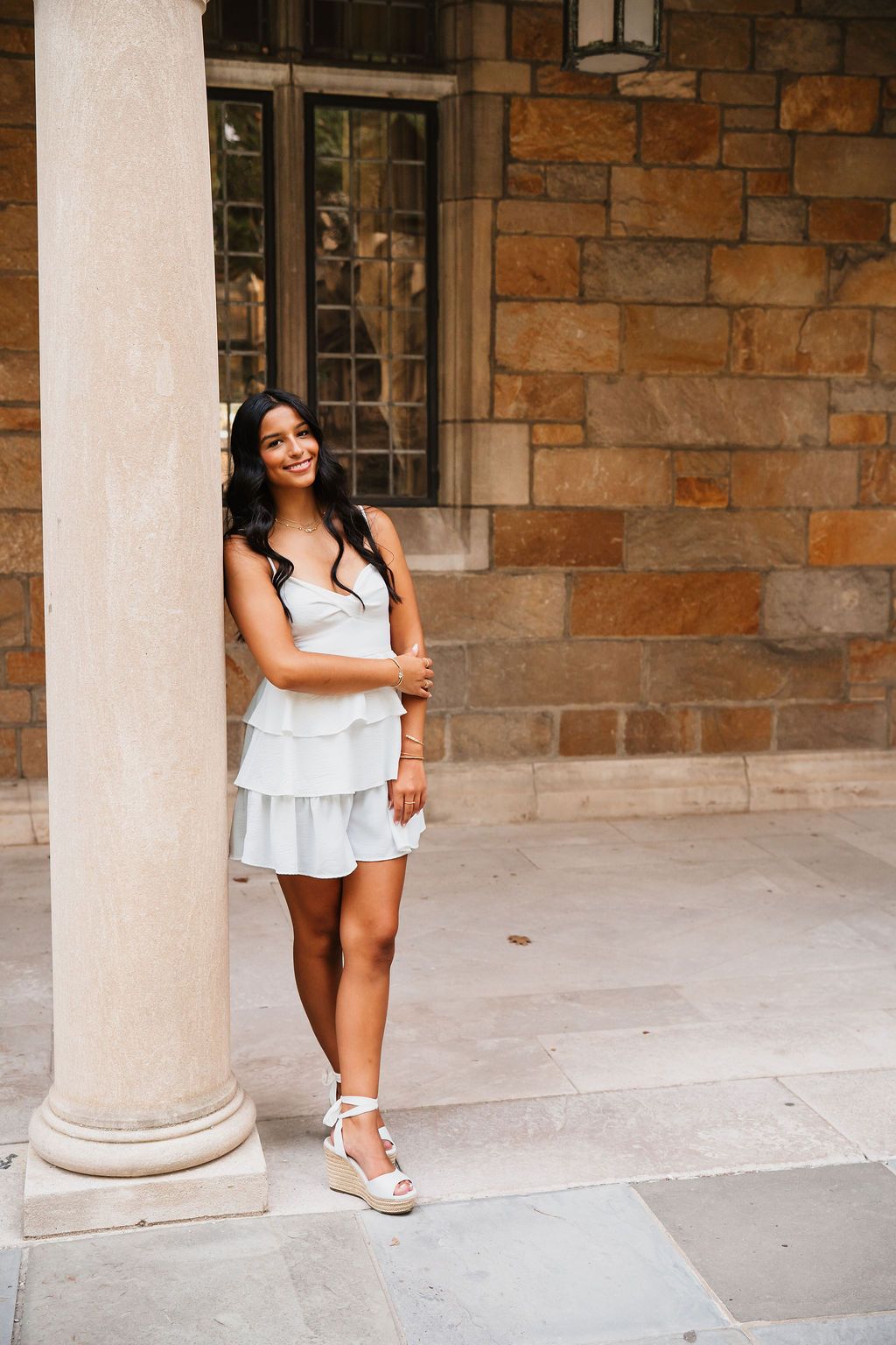 A person poses playfully between elegant stone columns in a classic architectural setting.