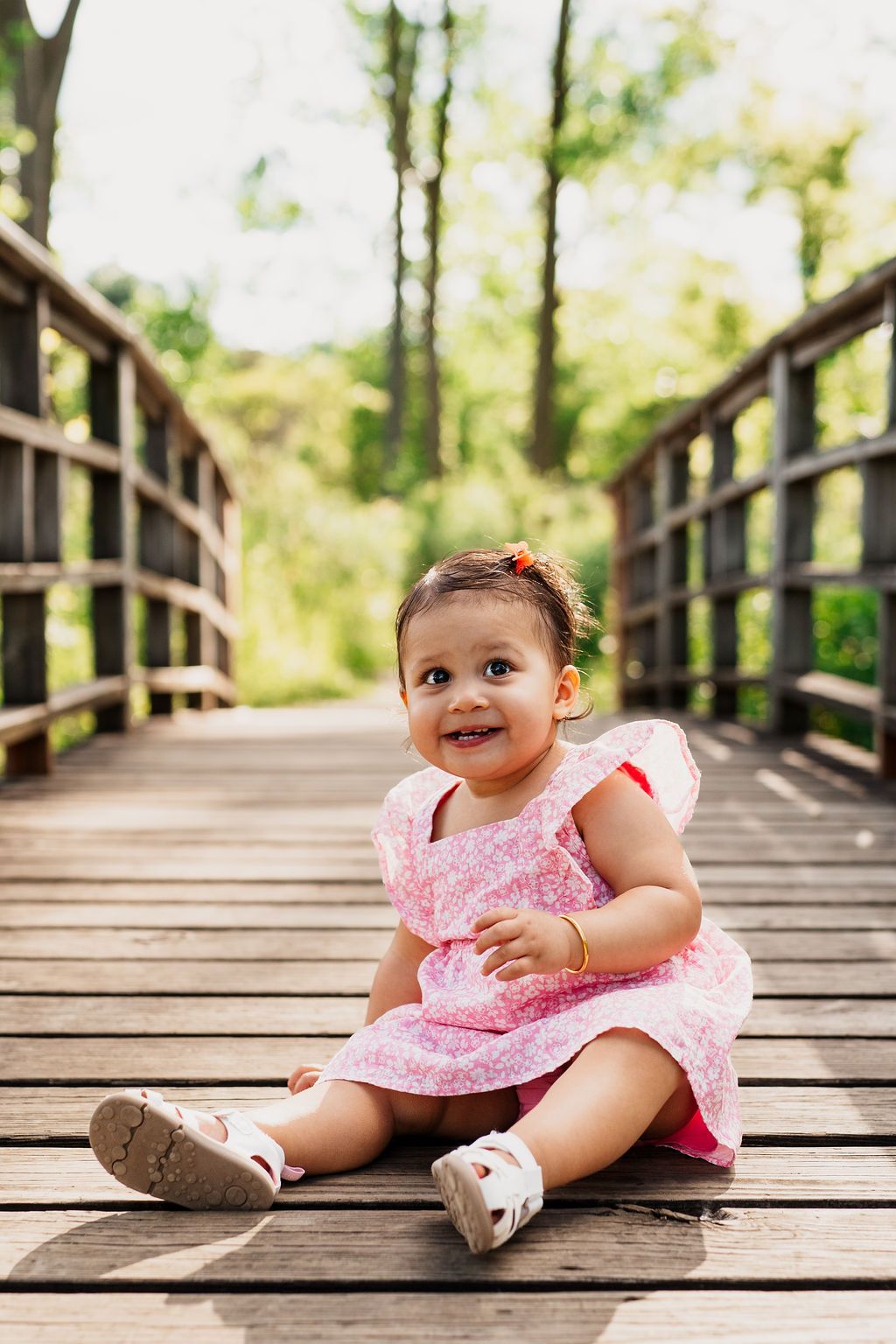 A baby in a pink dress sits on a wooden boardwalk in a series of progressive photos showing different expressions.