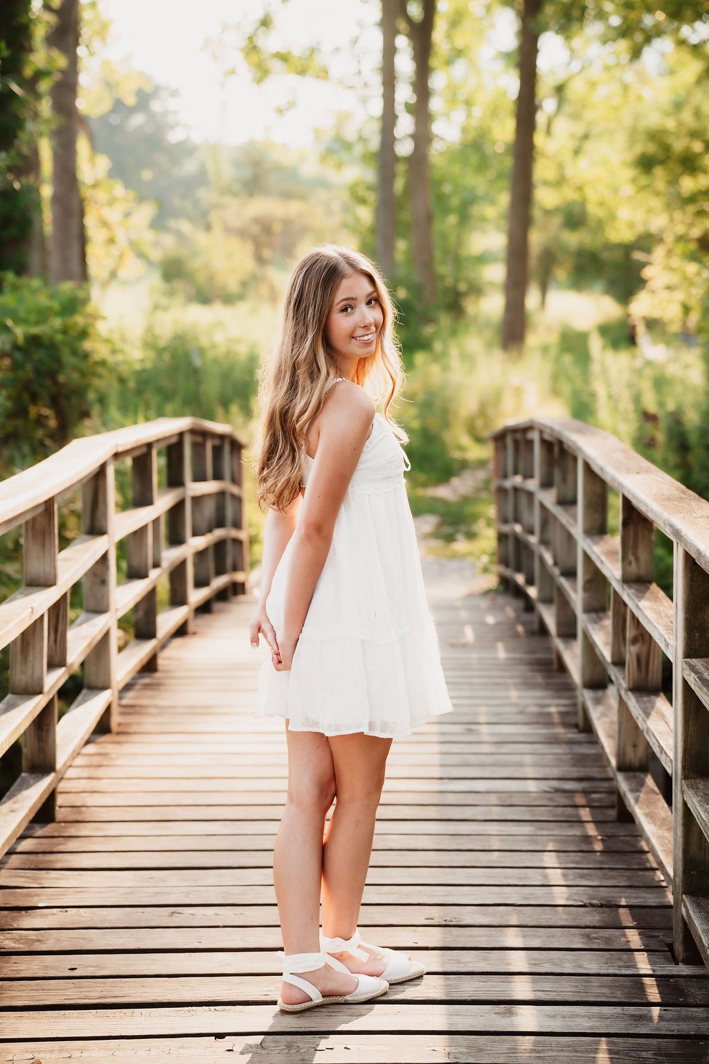 A series of photos showing a person in a white dress walking and posing on a wooden boardwalk in a sunlit forest setting.