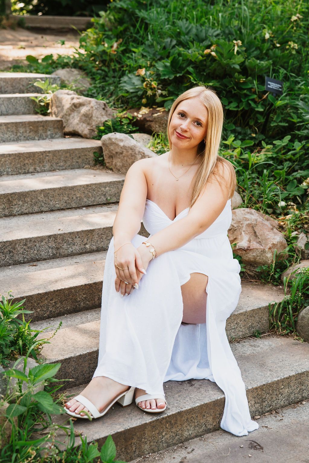 White dress portrait on stone garden steps surrounded by greenery.