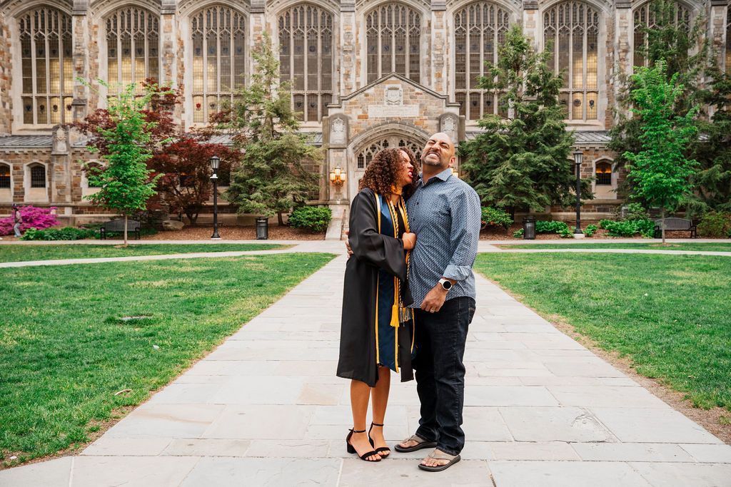 Couple shares a romantic moment on a stone pathway in front of a Gothic university building.