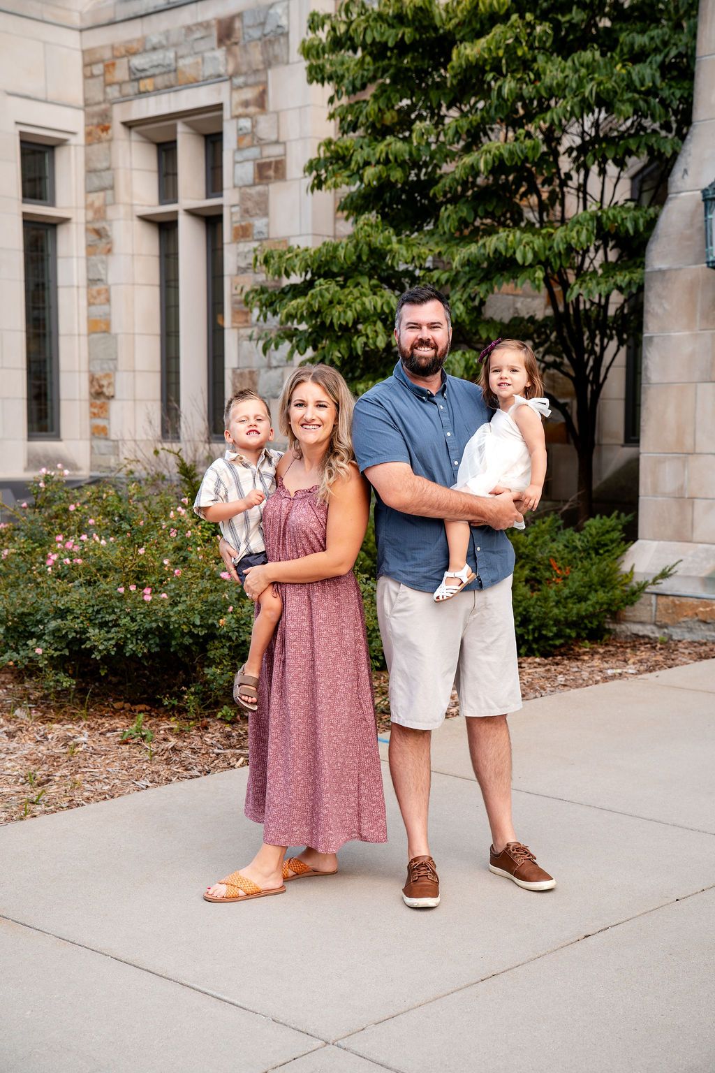 A family stands together on a stone building sidewalk wearing coordinated outfits in pink and neutral tones.