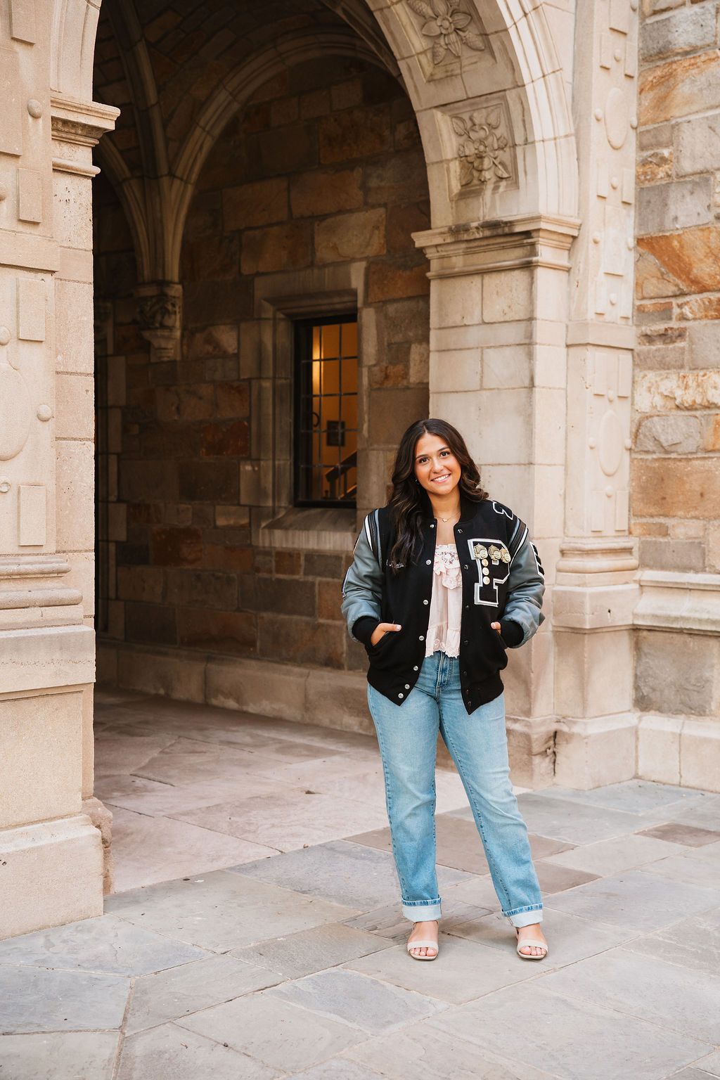 A person in a black jacket and jeans poses in a series of shots under stone archways of a historic building.