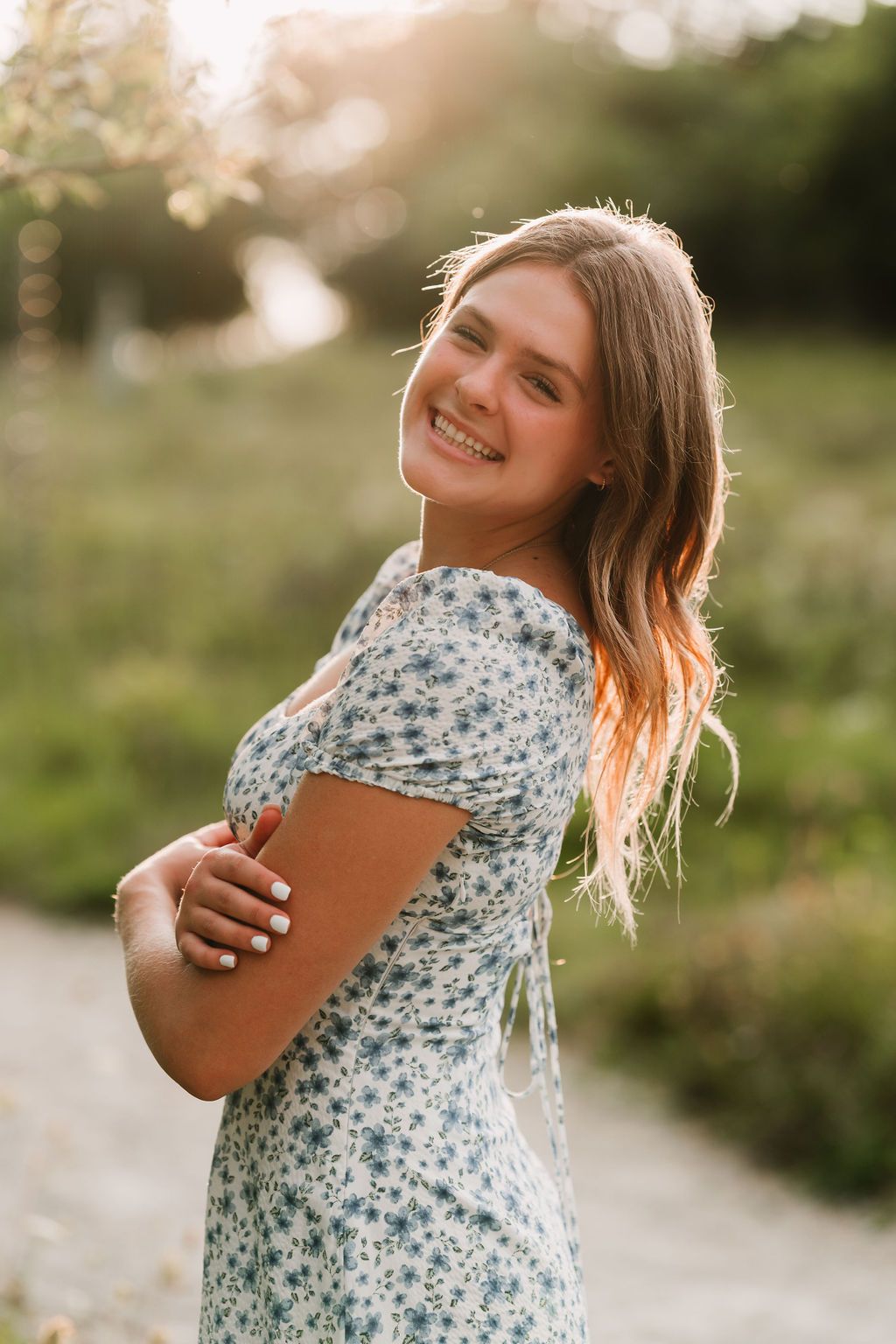 A person in a floral dress laughs joyfully while posing outdoors during golden hour.
