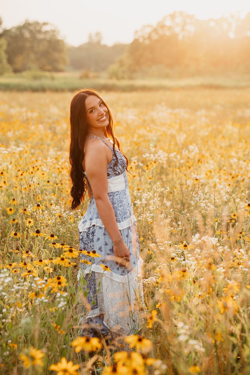 Figure in a summer dress poses joyfully among yellow wildflowers at sunset.