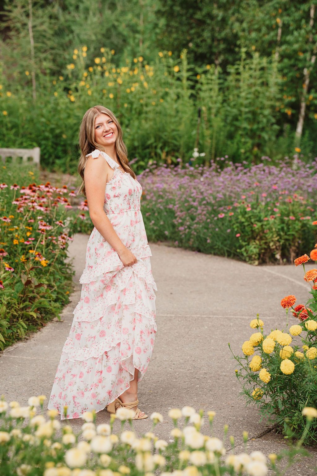 A floral garden path lined with colorful blooms including yellow, orange, and purple flowers on a sunny day.