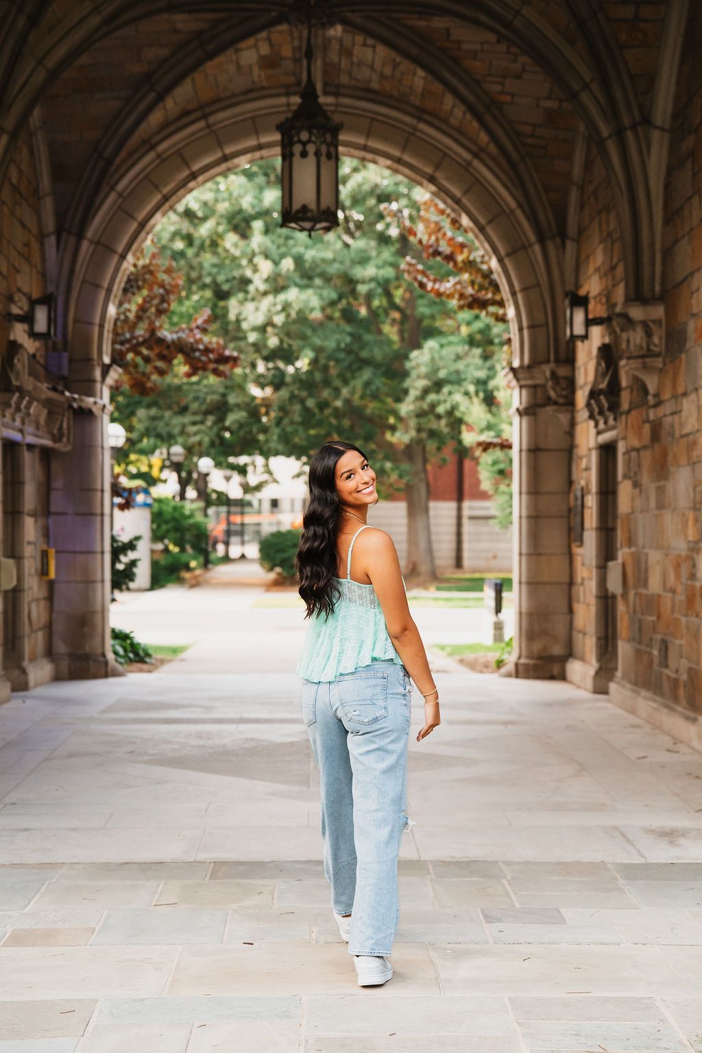 A figure dances and twirls joyfully beneath a grand stone archway on a university campus.