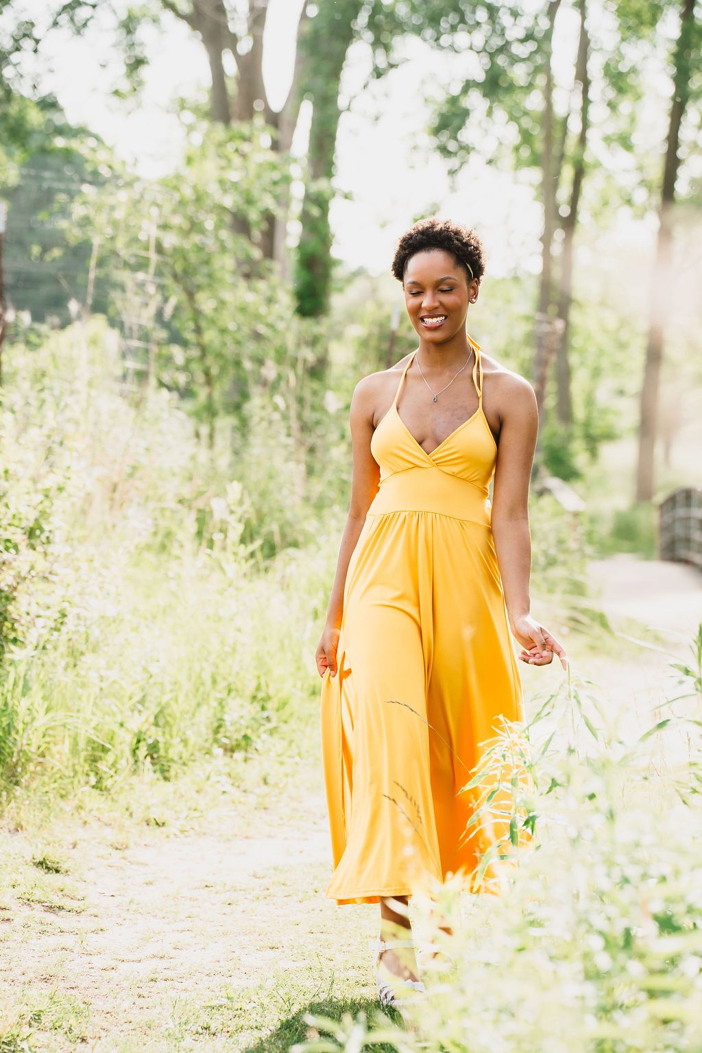 A bright yellow sundress flows elegantly as someone walks along a sunlit forest path on a summer day.