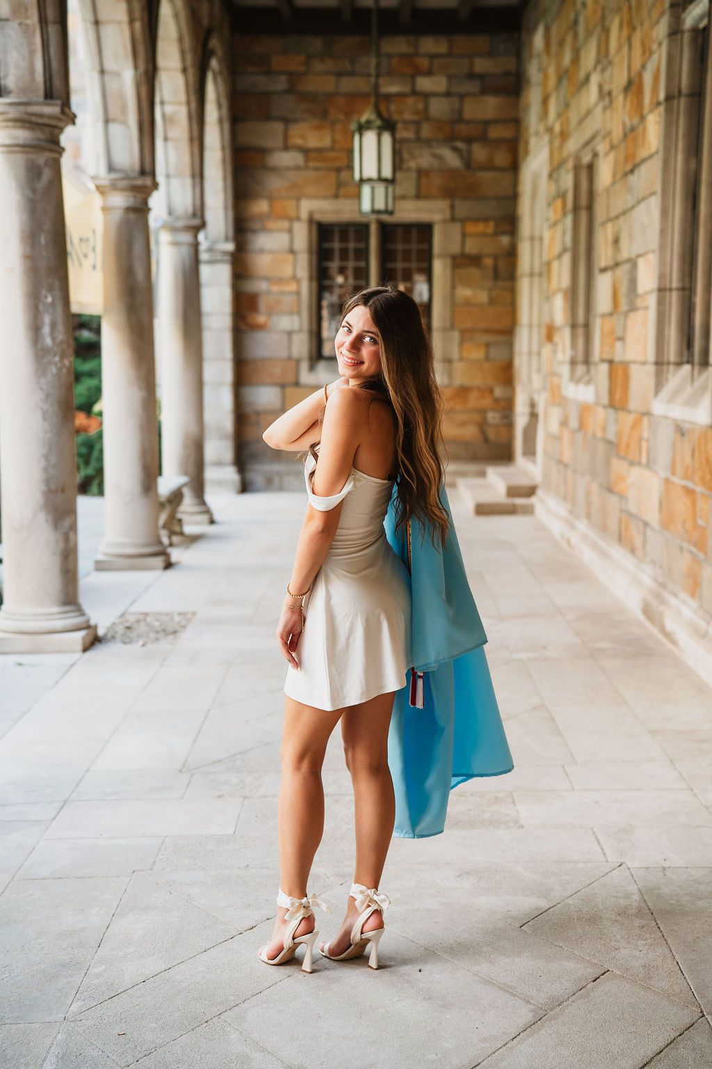 Woman in white dress twirls playfully in an ornate stone colonnade with natural lighting.
