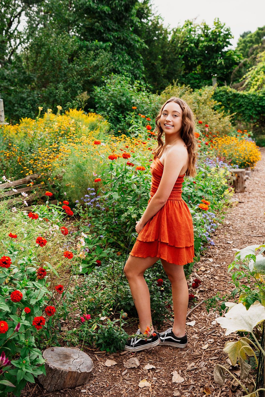 A garden pathway lined with bright red and orange flowers surrounded by verdant summer foliage.