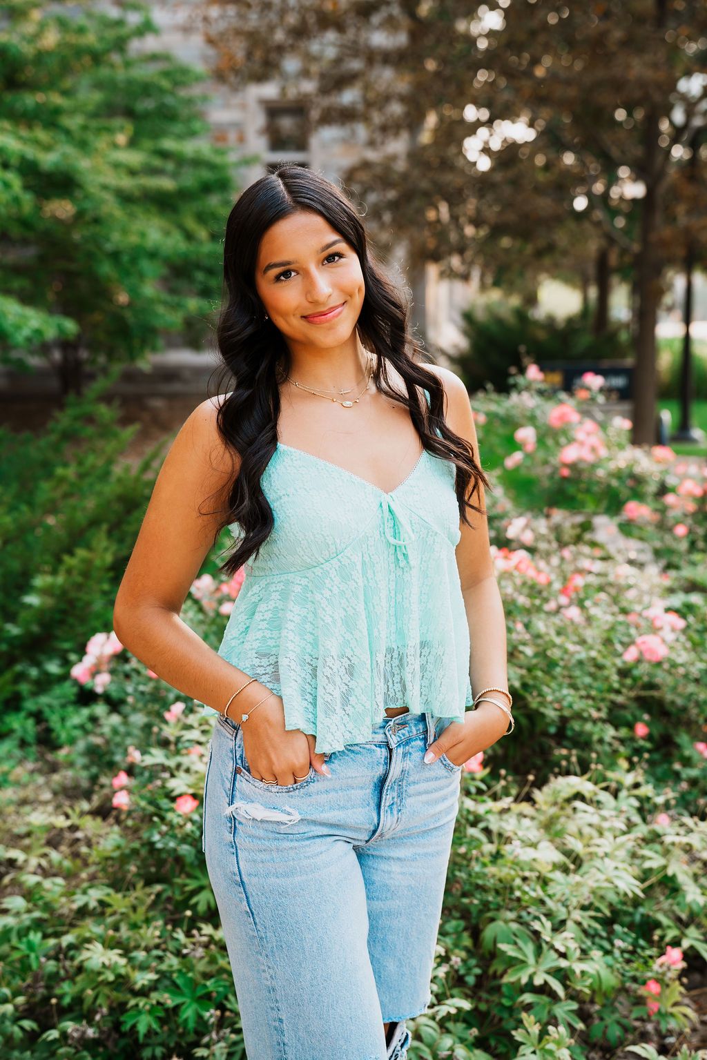 A summery outfit featuring a light blue ruffle top and high-waisted jeans photographed in a garden with pink flowers.