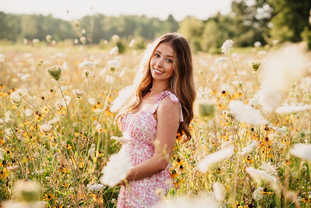 A pink floral dress stands out in a golden wildflower meadow during sunset with soft summer lighting.