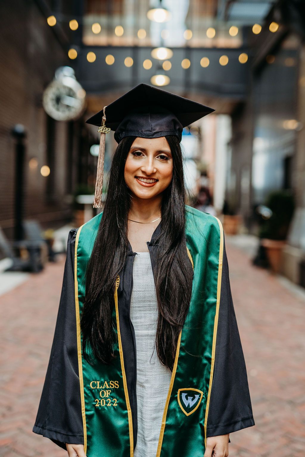 College graduate wearing emerald green graduation stole and black cap poses for graduation photos outdoors.
