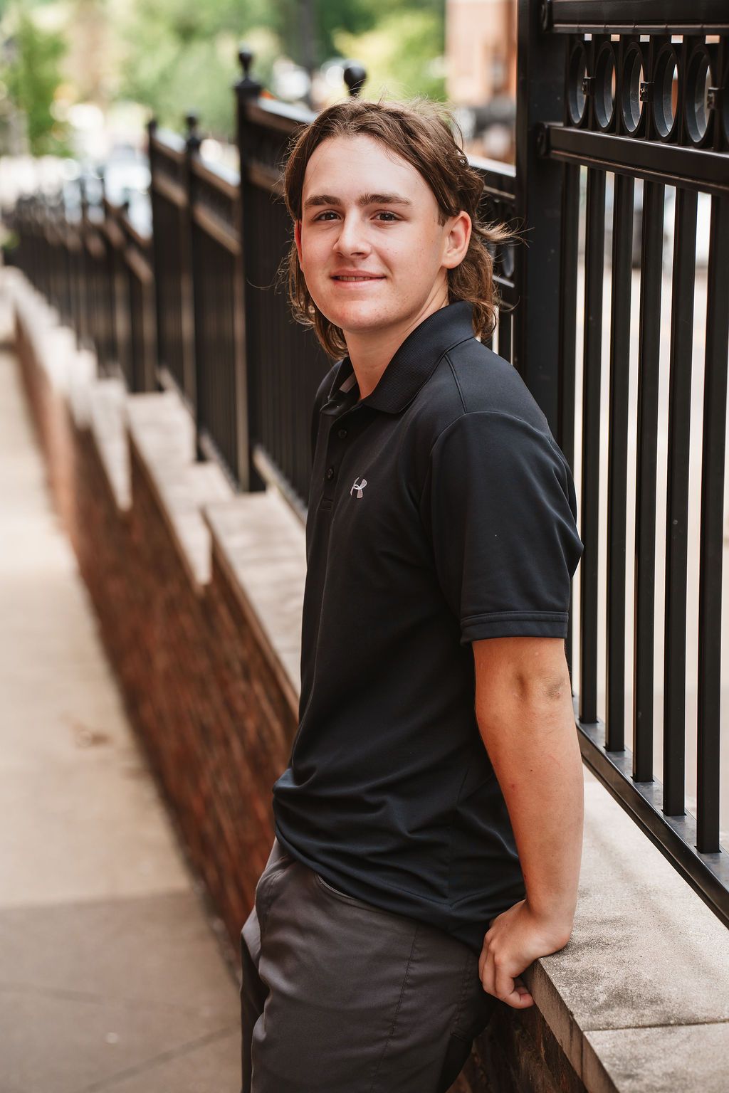 A series of casual portraits against a brick wall and railing showing different poses in a black shirt.