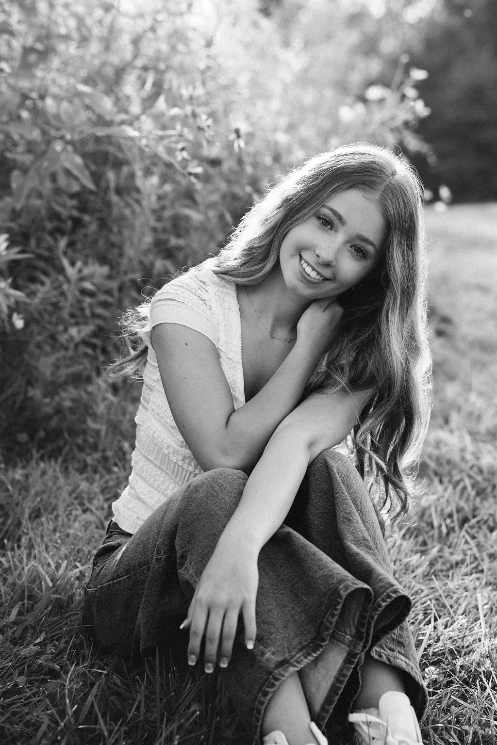 Black and white portrait series of someone lying in grass wearing a white top and jeans in a relaxed outdoor setting.