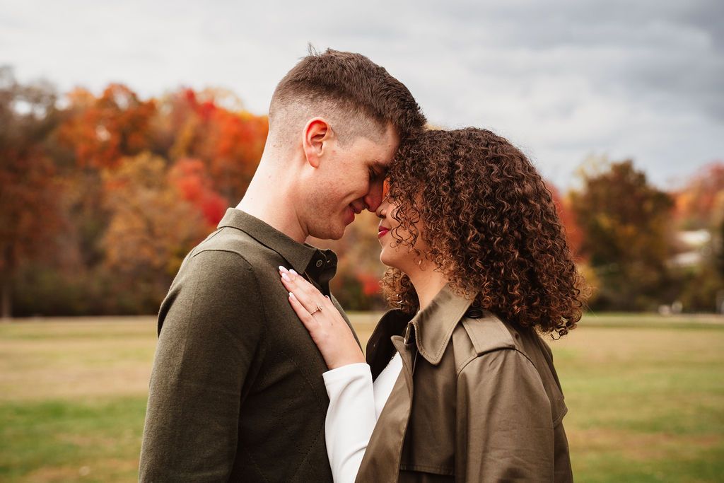 Romantic couple sharing an intimate moment outdoors in autumn park with colorful fall foliage in background.