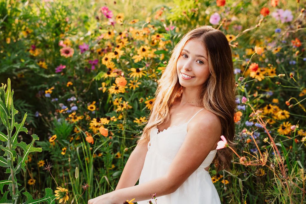 Senior portrait session in white dress surrounded by colorful summer wildflowers.