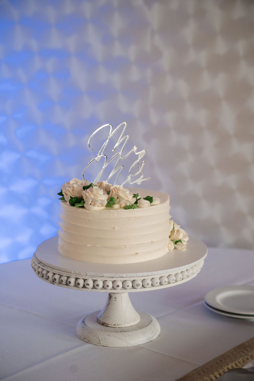 Elegant white wedding cake with simple floral decorations on decorative stand.