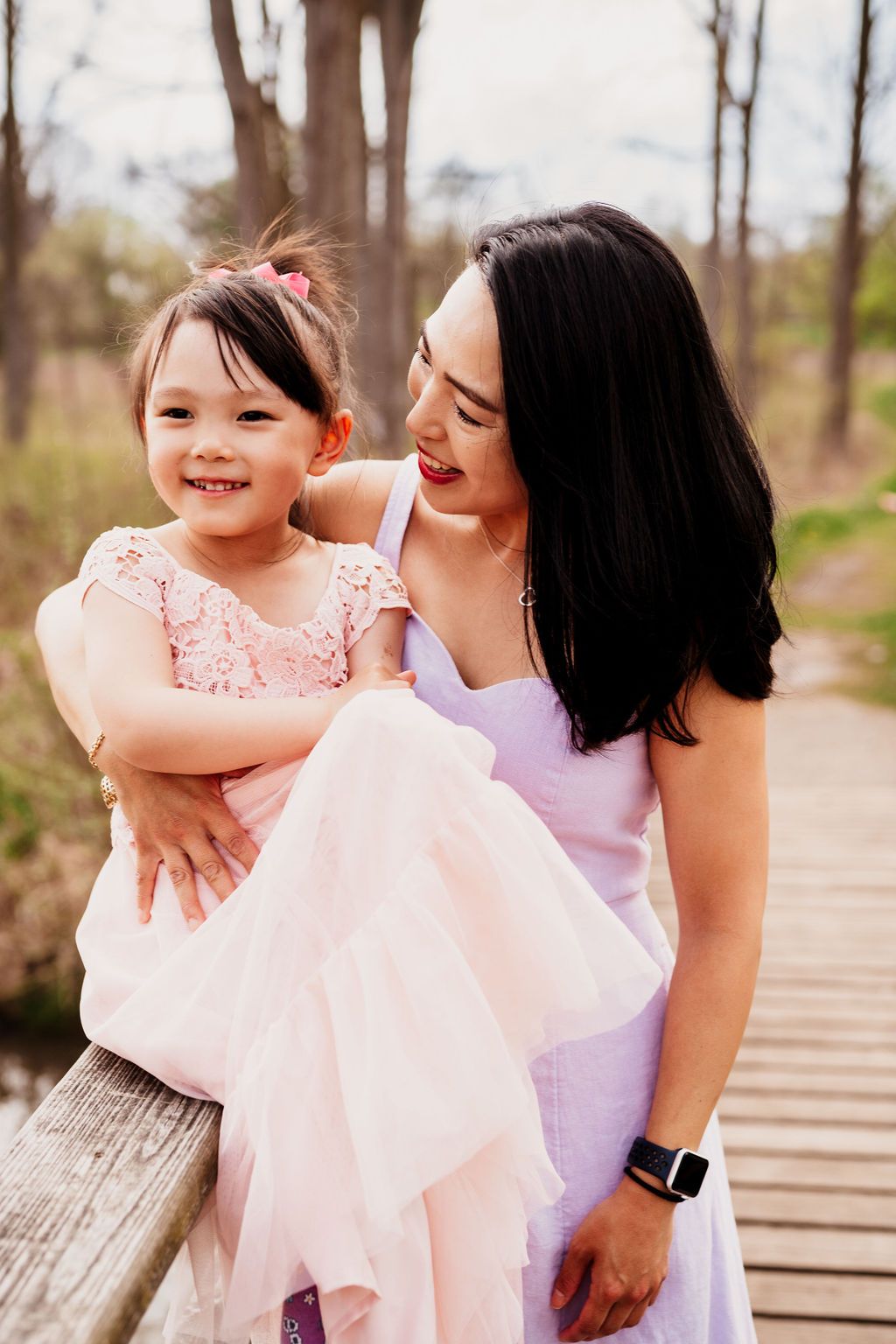 A parent and child share tender moments together on a wooden boardwalk while wearing pink and purple outfits.