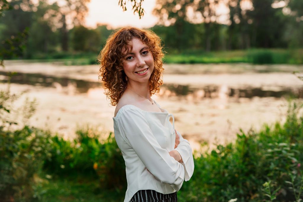 A rustic outdoor photo session at golden hour featuring someone in a white top amidst natural greenery.