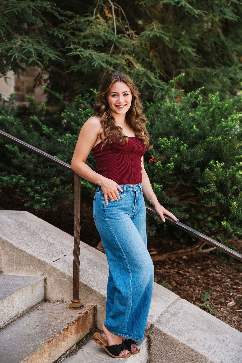 A series showing someone in burgundy top and jeans posing on outdoor stone steps near greenery.