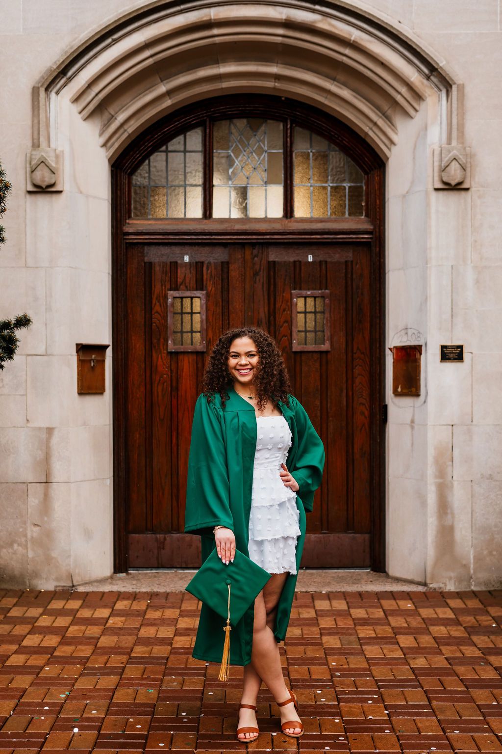 A person in a green blazer poses in front of an ornate stone archway with wooden doors and brick flooring.