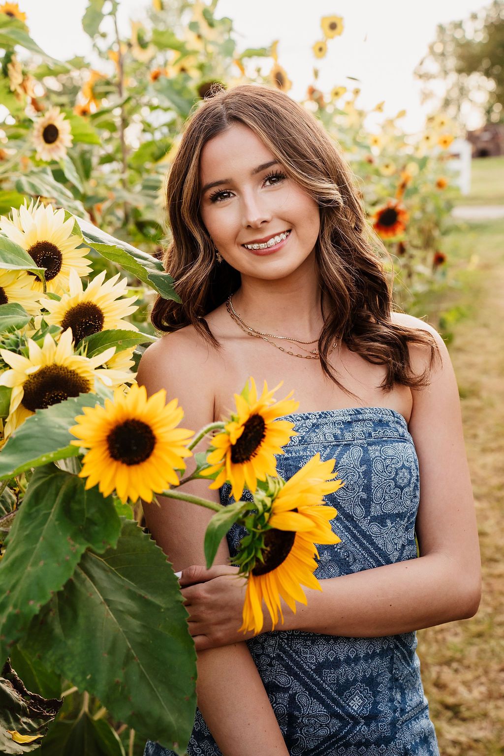 A summer portrait in a sunflower field featuring a blue patterned dress against vibrant yellow blooms. Plymouth Orchards Sunflowers Michigan
