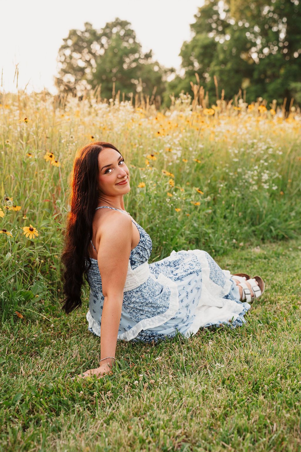 Person in a blue and white dress lying in grass among yellow wildflowers during golden hour.