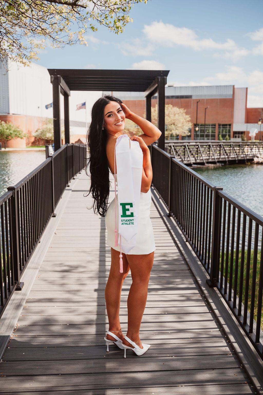 Young woman in white Eastern Michigan University Student Athlete dress posing on a wooden bridge.