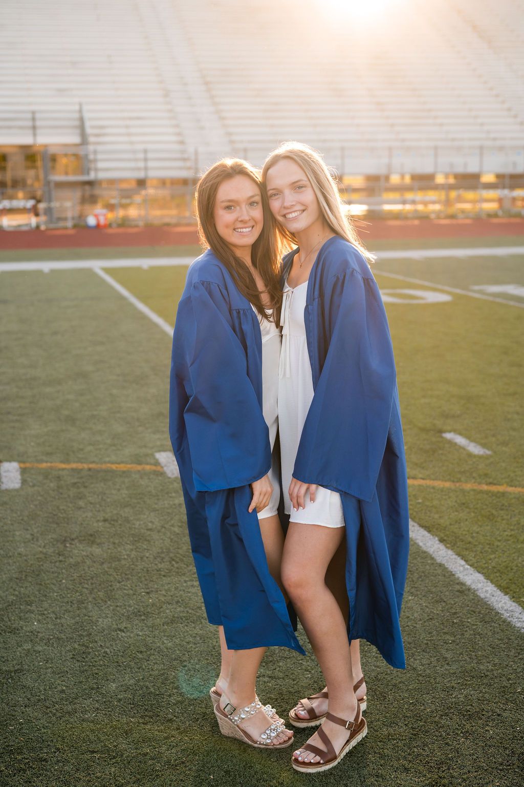 Two people in blue blazers stand together on a football field during golden hour sunset.