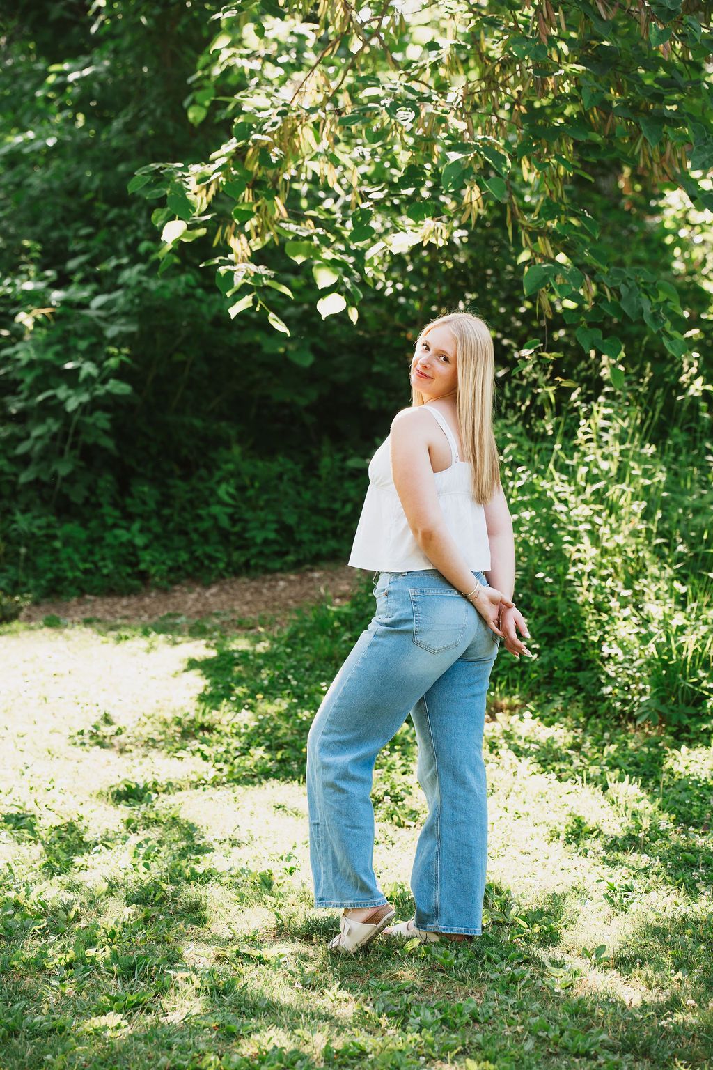 Person in casual wear posing playfully in a lush green garden setting.