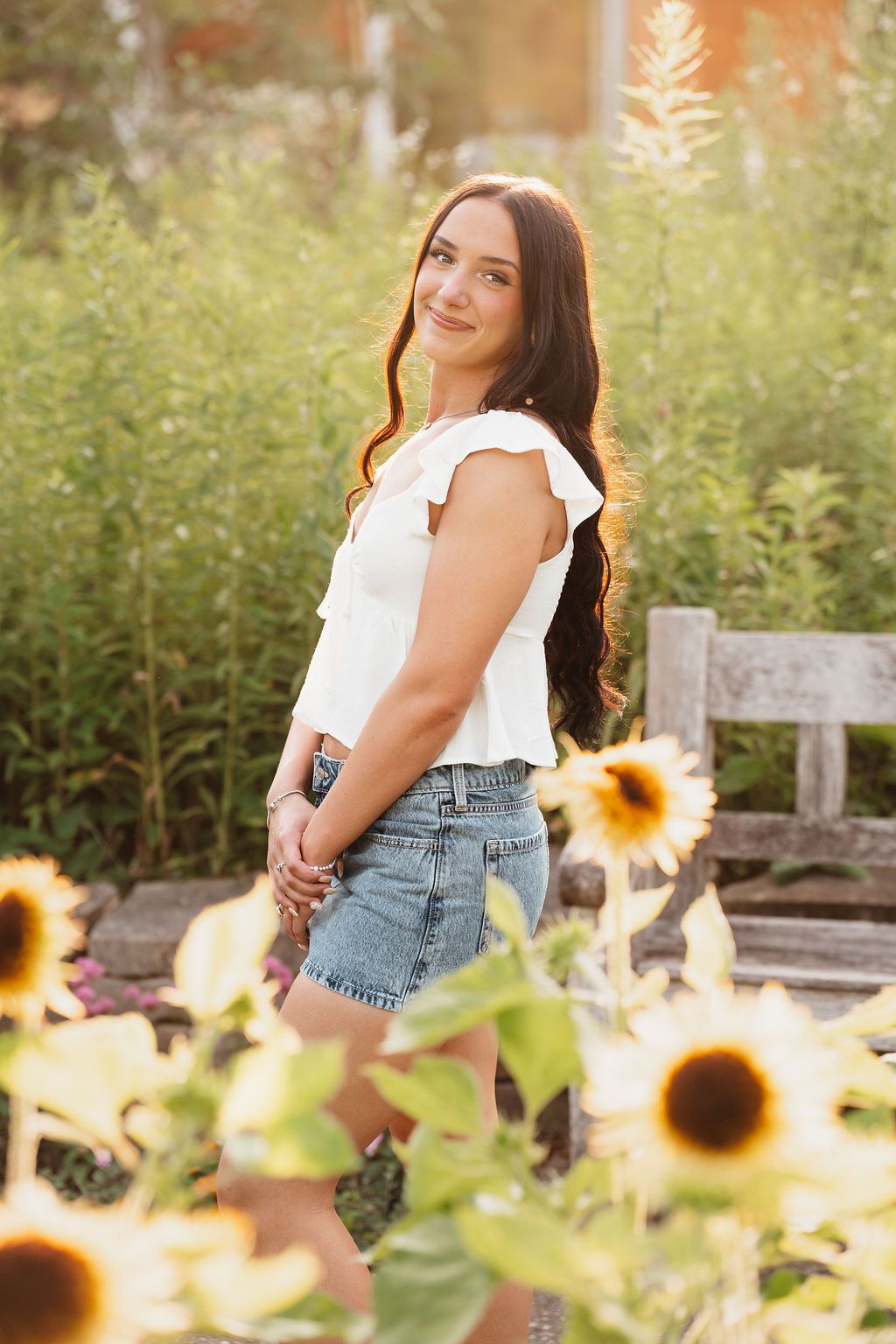 Rustic wooden bench surrounded by blooming sunflowers in a garden setting.