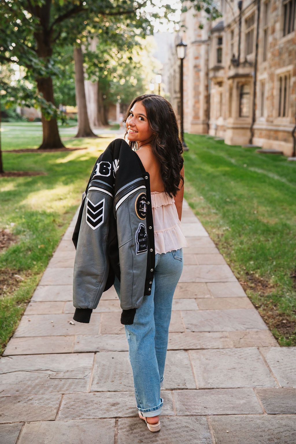 Playful poses with varsity jacket against stone building exterior.