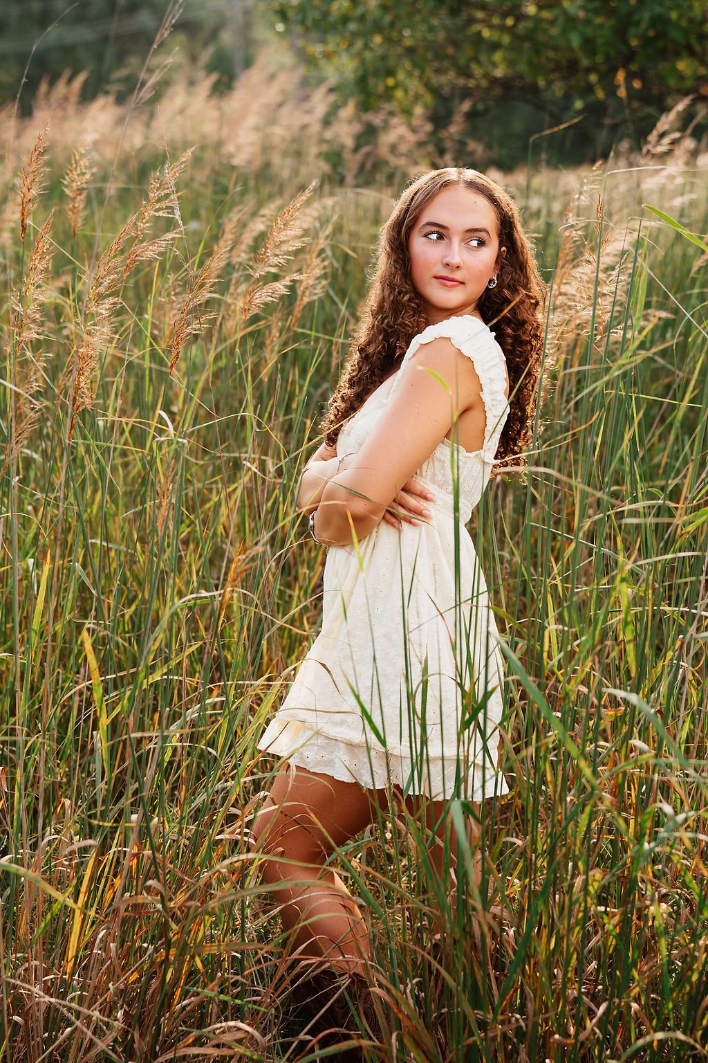 A dreamy outdoor portrait session in tall golden grass during sunset with soft natural lighting and vintage styling.