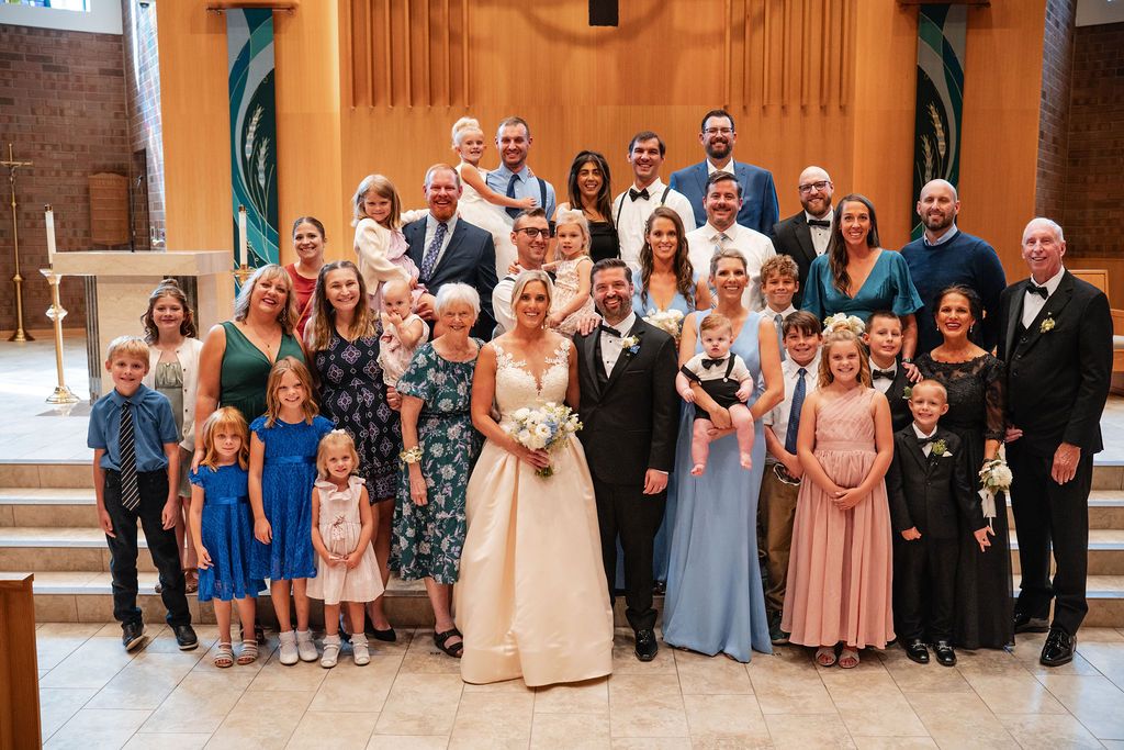Large wedding party group photo with guests in formal attire standing together in coordinated blue and pink dresses.