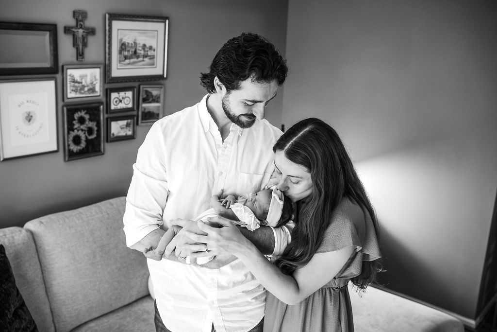 Black and white photo of new parents lovingly gazing at their newborn baby in a cozy home setting.