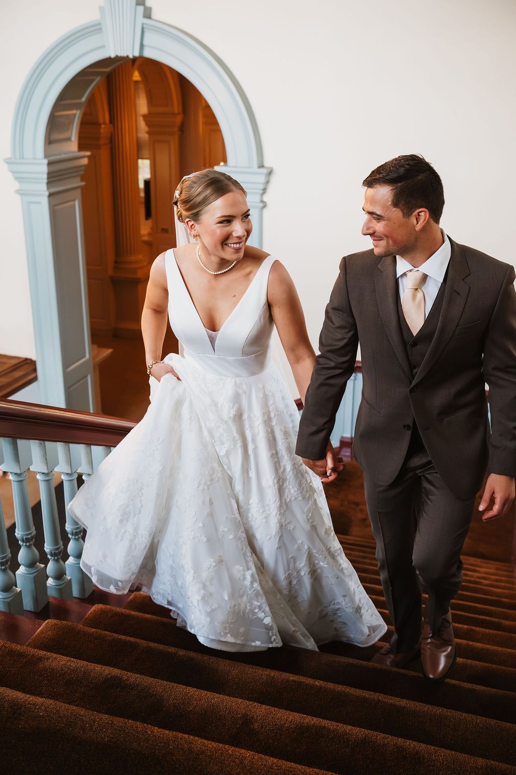 Couple descending grand staircase in formal wedding attire at historic venue.
