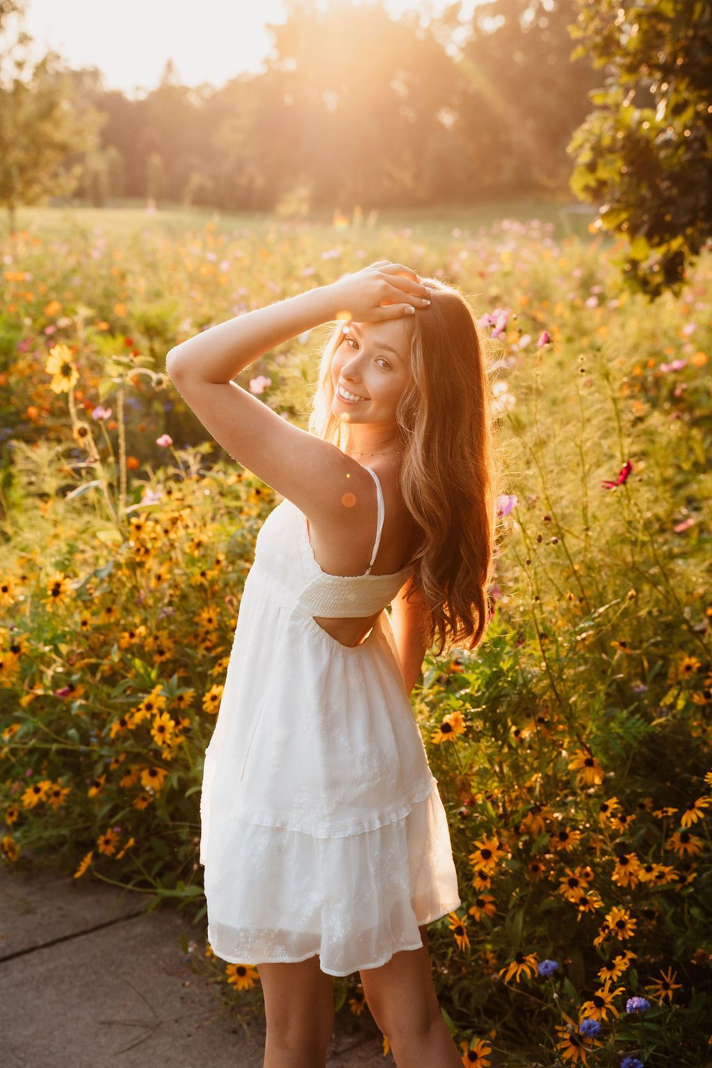 A dreamy summer portrait in a white dress against a golden sunset garden with blooming flowers.