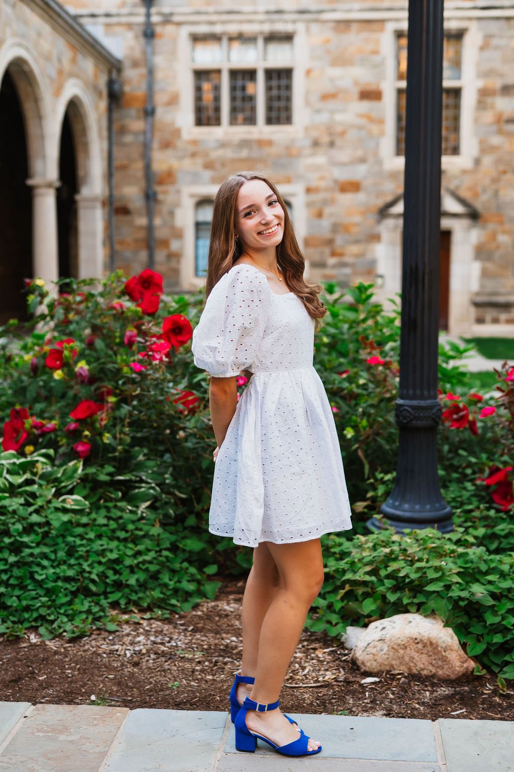 A white lace dress and blue heels are shown in a series of photos against a stone building and rose garden backdrop.