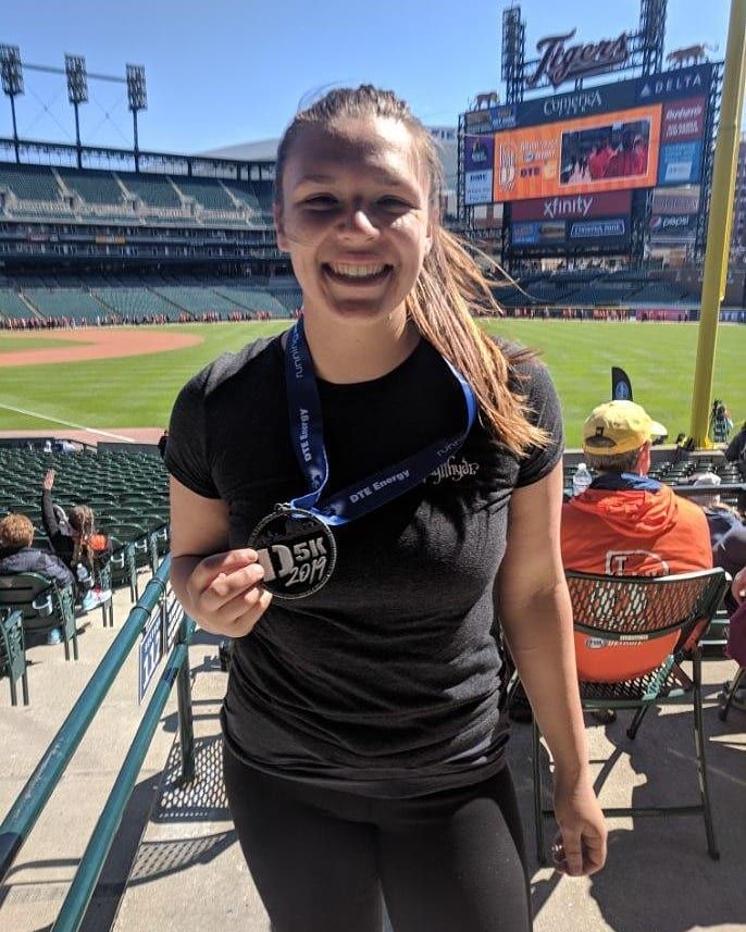 Woman proudly displaying a 5K race medal at Comerica Park, home of the Detroit Tigers baseball stadium.