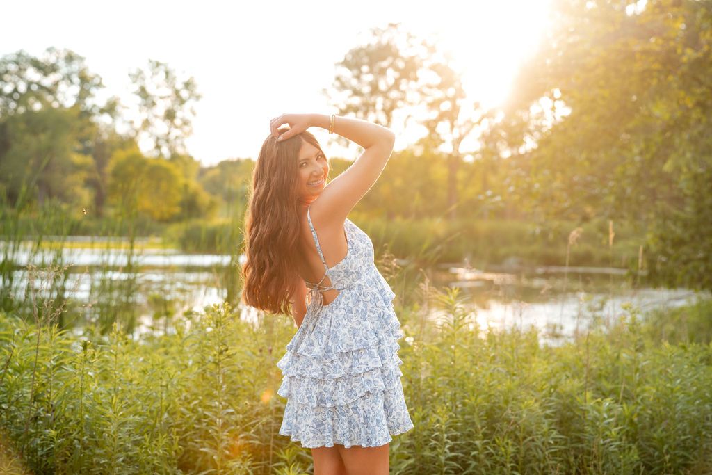Person in white dress enjoying sunset by lake among wildflowers. Senior photos at Matthai botanical gardens, PCEP Senior Photos