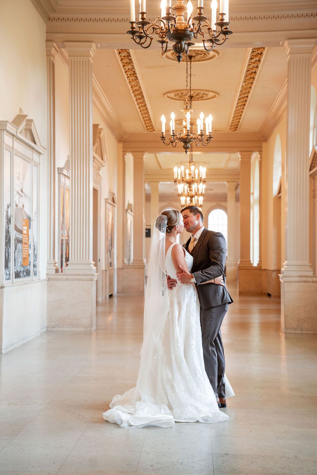 Wedding couple sharing intimate moments in grand ballroom with ornate details and chandeliers.
