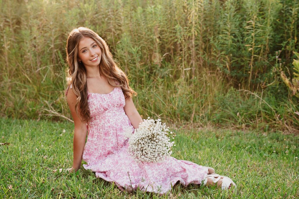 A person in a pink floral dress poses gracefully in a lush green meadow with wildflowers and tall grass.