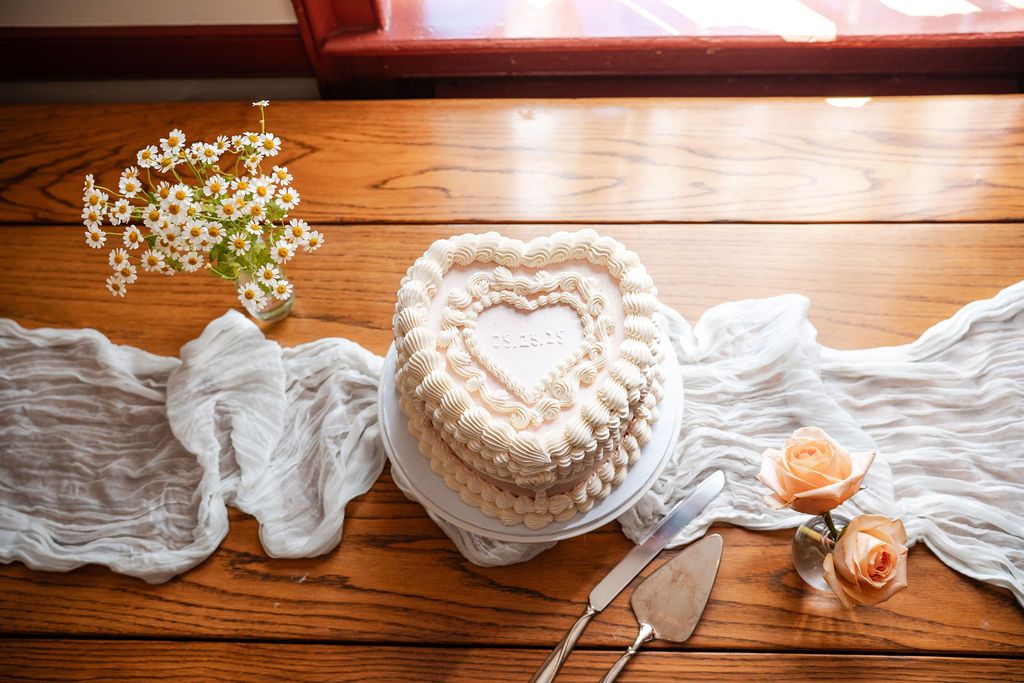 Wedding details with lace veil and heart-shaped cake on rustic wooden table.